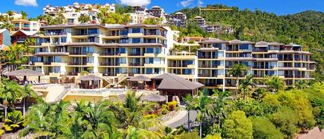 A multi-story hotel with balconies, a pool area, and lush greenery.