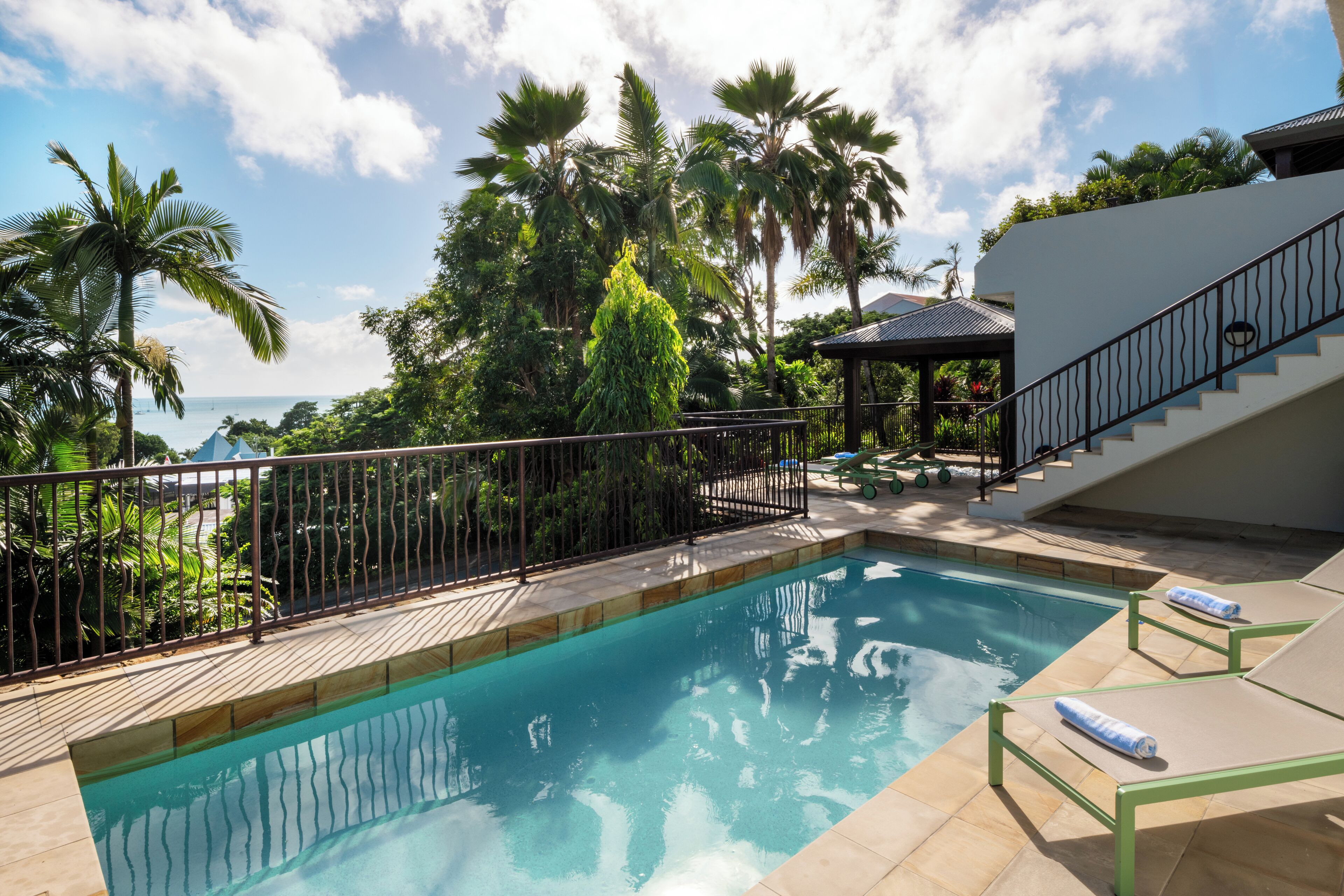 A swimming pool with a metal fence, lounge chairs, and a staircase leading to an upper level.