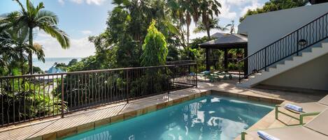 A swimming pool with a metal fence, lounge chairs, and a staircase leading to an upper level.