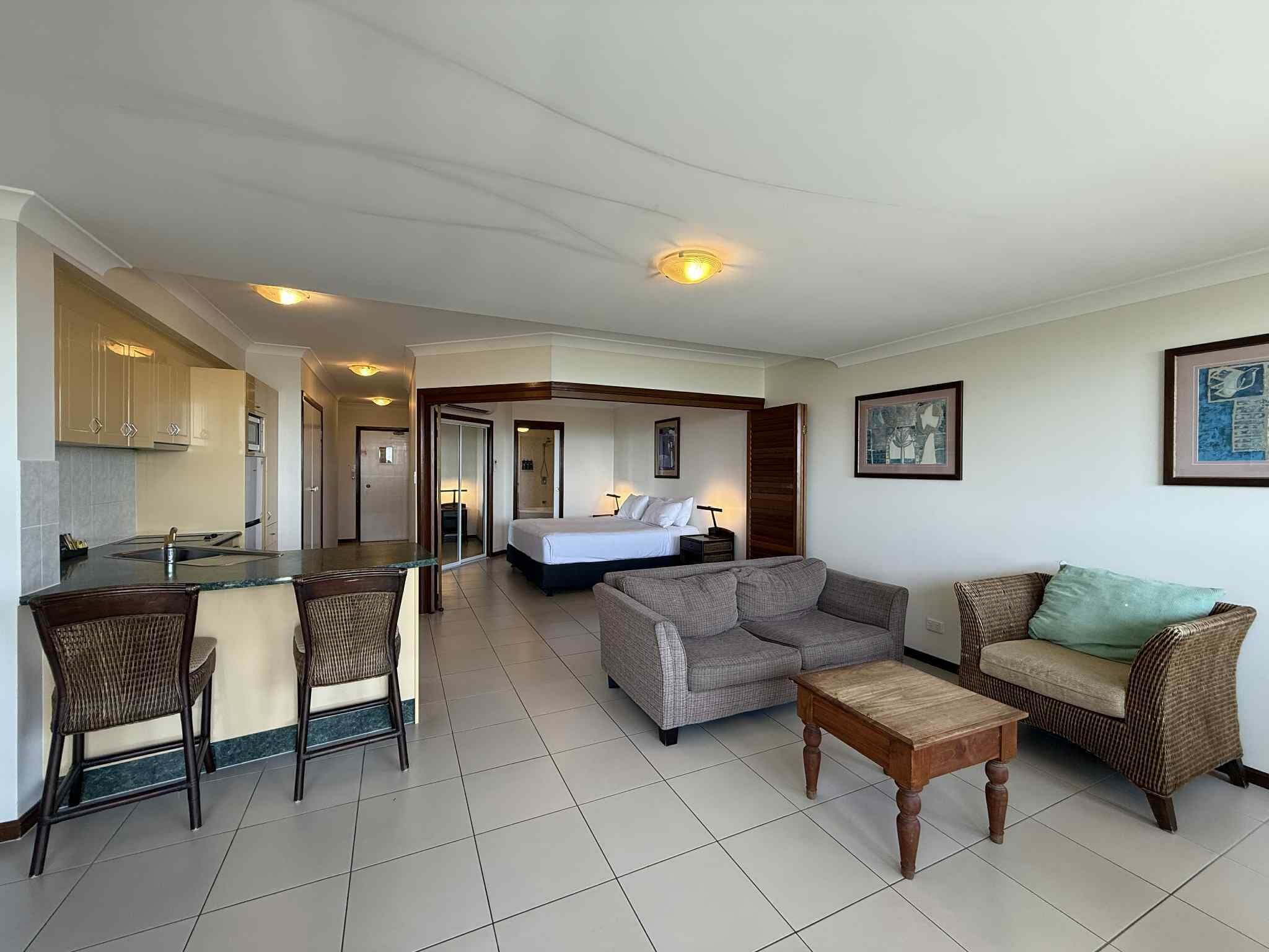A hotel room with a kitchenette, a bed, a sofa, and a dining area.