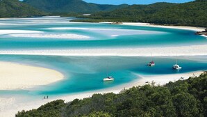 A coastal landscape with clear turquoise waters, a sandy beach, and boats anchored near the shore.