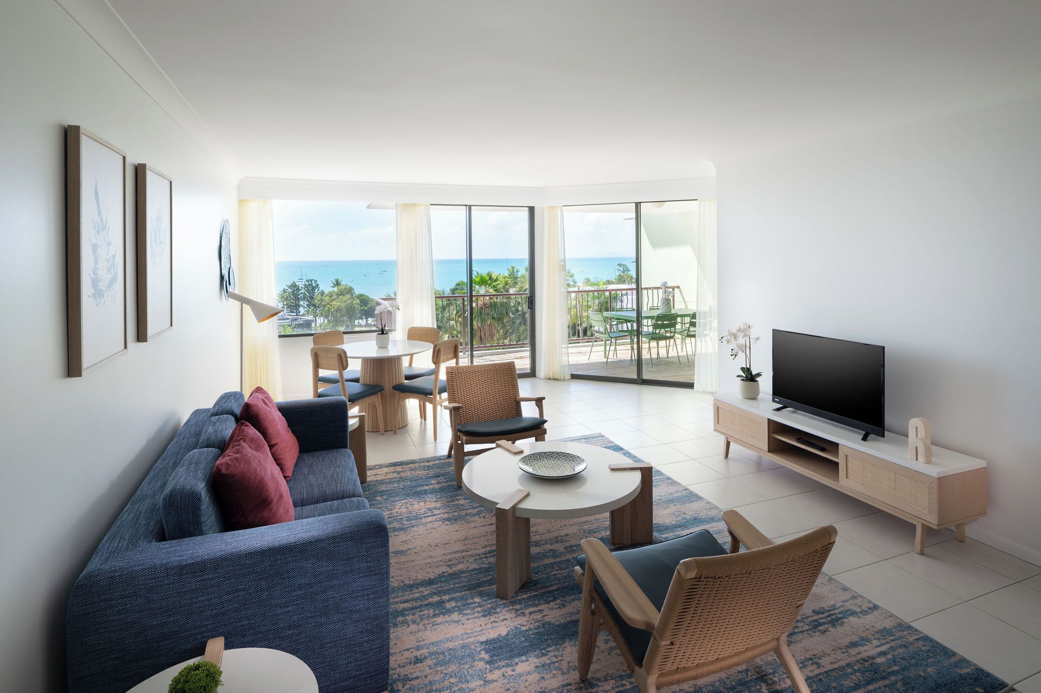 Een moderne woonkamer met een bank, stoelen, een televisie en een balkon met uitzicht op de oceaan.