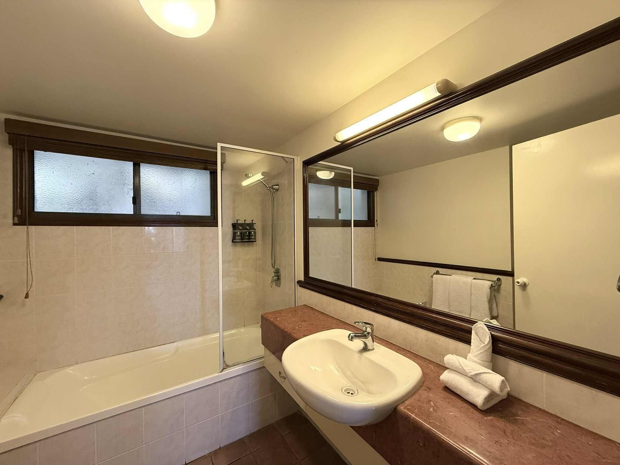 A modern bathroom with a bathtub, a shower, a sink, and a large mirror.