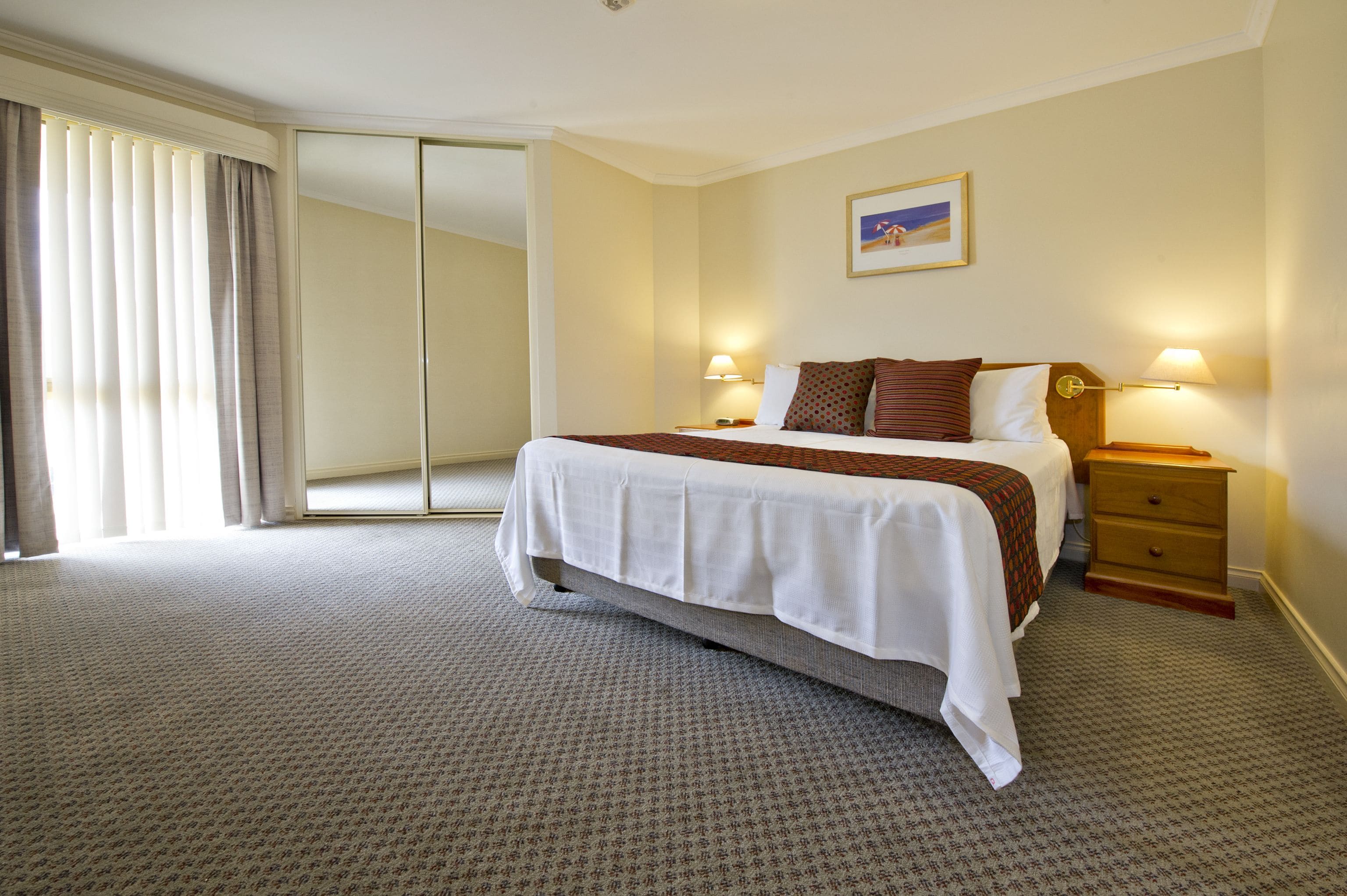 A hotel room with a large bed, two bedside tables with lamps, a sliding door, and a framed picture on the wall.