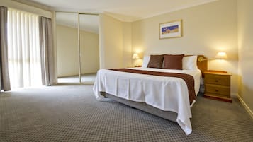 A hotel room with a large bed, two bedside tables with lamps, a sliding door, and a framed picture on the wall.