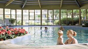 An indoor swimming pool with clear glass walls, a covered roof, and a poolside area with chairs and flowers. - Abbey Beach Resort (Broadwater)