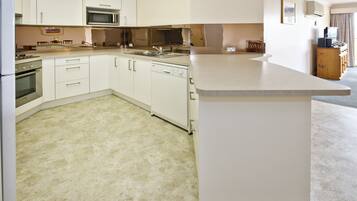 A compact kitchen with white cabinets, a microwave, an oven, and a dishwasher.
