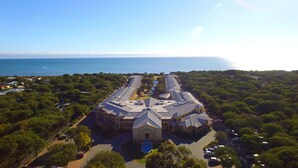 An aerial view of a hotel with a central building surrounded by lush greenery, a swimming pool, and a view of the sea. - Abbey Beach Resort (Broadwater)