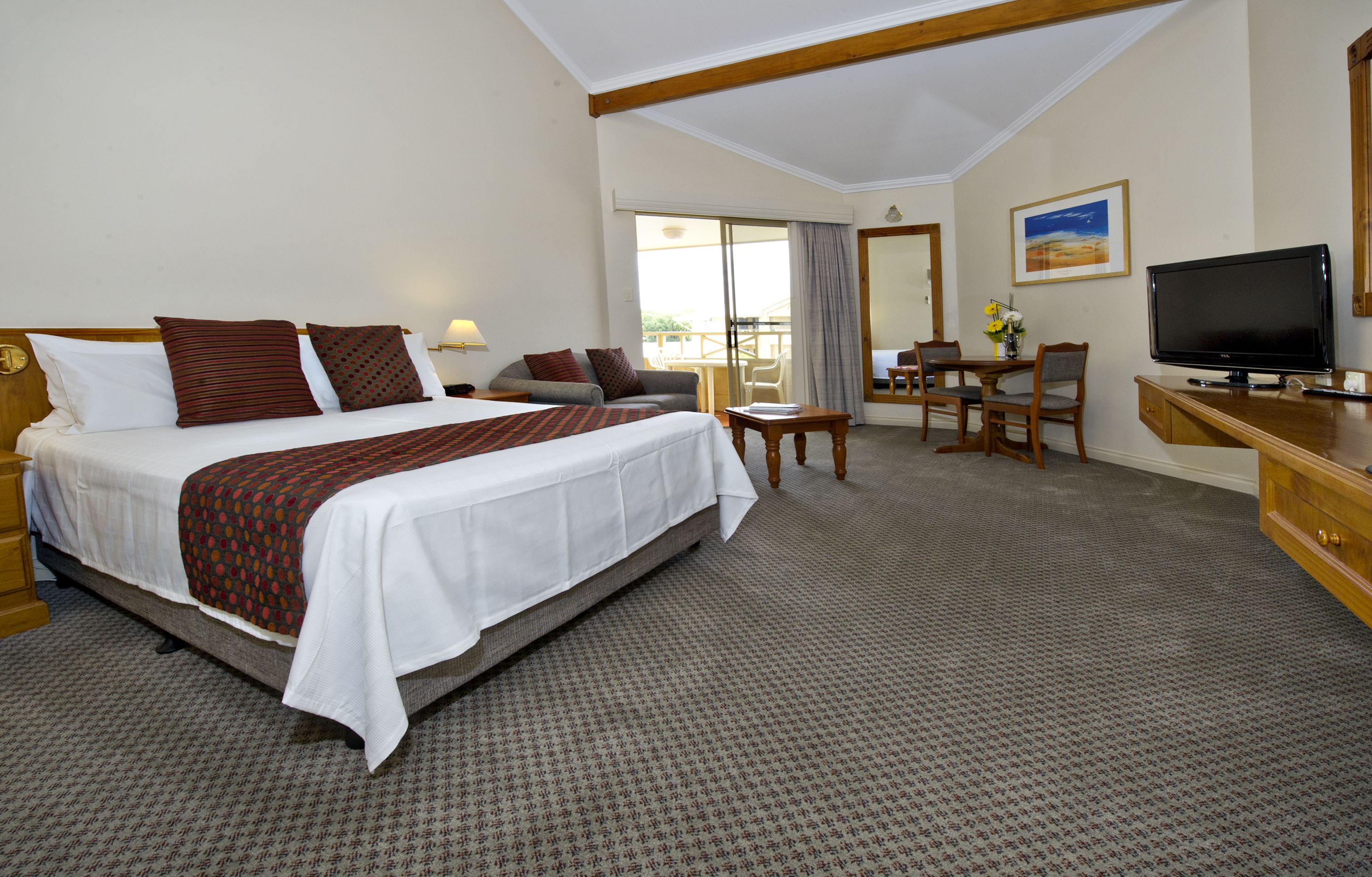 A hotel room with a large bed, a desk with a chair, a television, and a balcony with a view.
