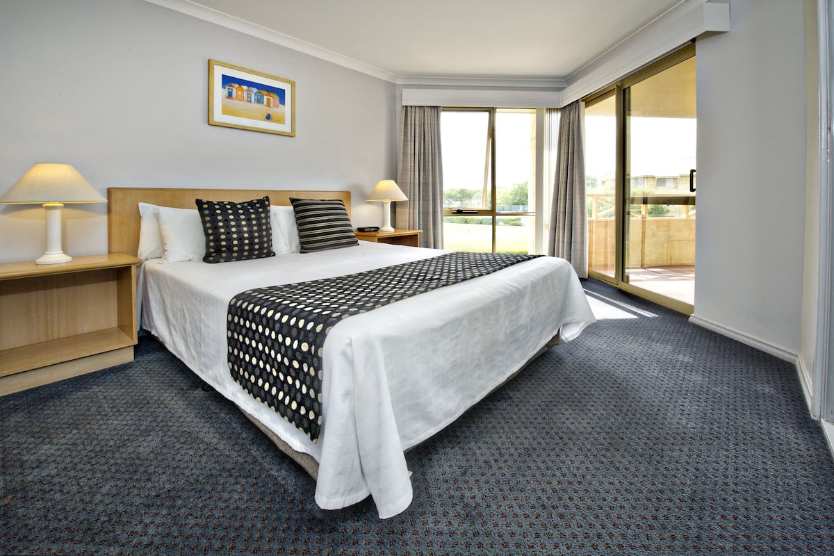Habitación de hotel con una cama grande, dos mesitas de noche con lámparas, una ventana con vistas y un cuadro en la pared.