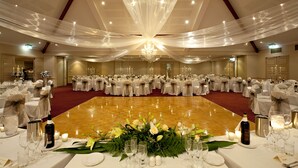 A banquet hall with round tables set for a formal event, featuring chandeliers and floral centerpieces. - Abbey Beach Resort (Broadwater)