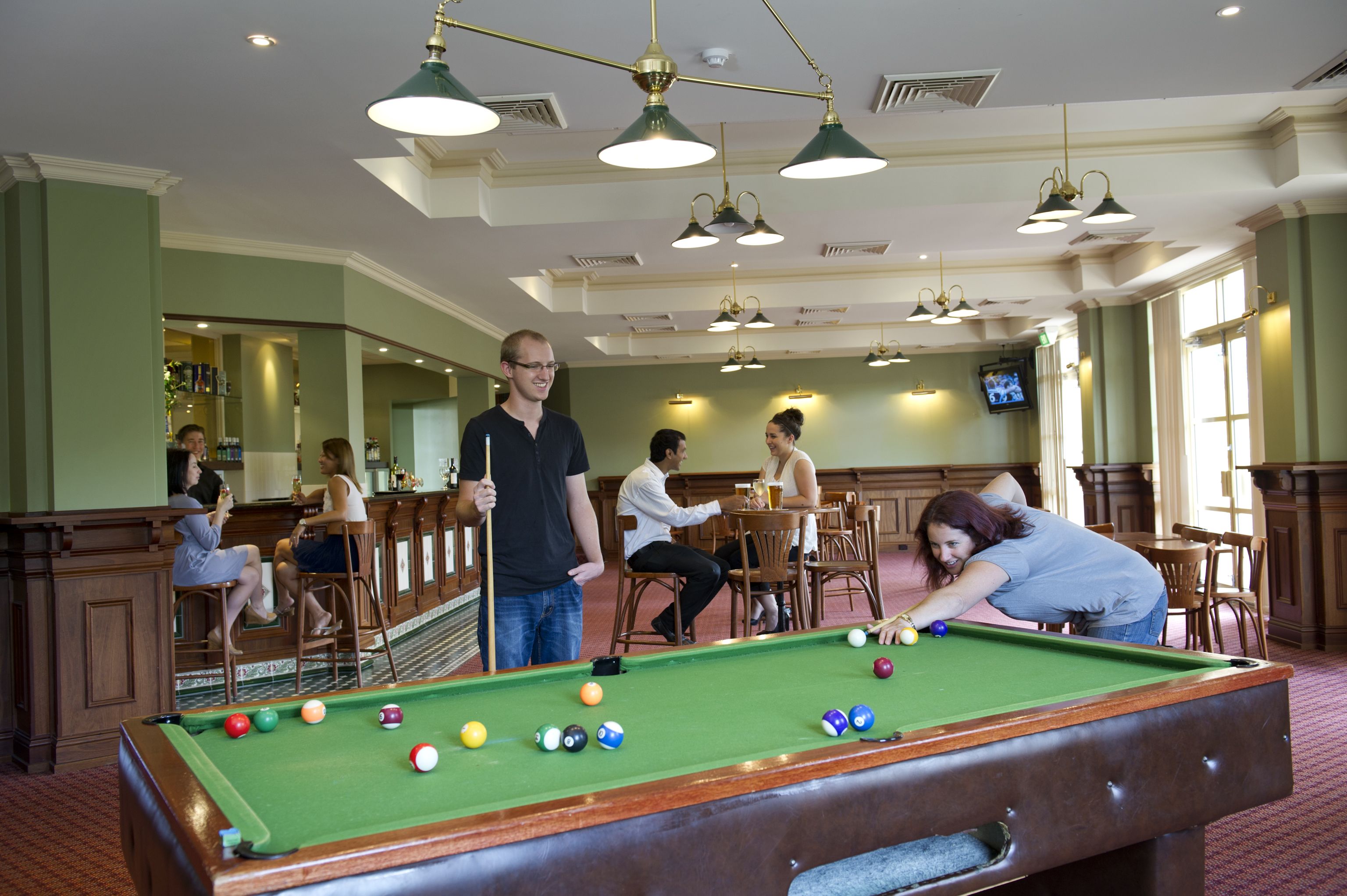 A pool table in a room with green walls and wooden furniture.