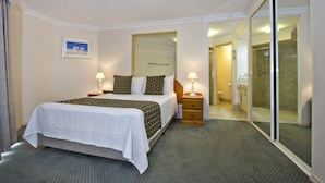 A hotel room with a bed, bedside lamps, a framed picture on the wall, and a sliding glass door leading to a bathroom. - Abbey Beach Resort (Broadwater)