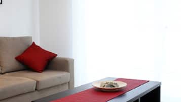 Een moderne woonkamer met een bank, een zwarte salontafel met een rode loper en een groot raam dat voor natuurlijk licht zorgt.