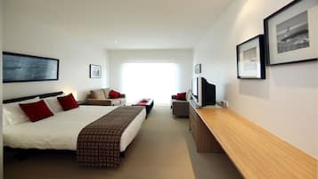 Een hotelkamer met een groot bed, een bureau, een stoel en een televisie. Er zijn twee ramen en een deur.