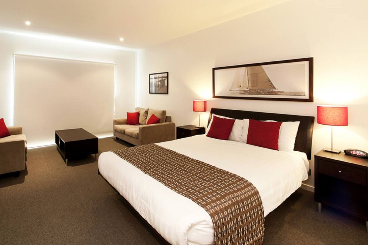 A hotel room with a large bed, two armchairs, a small table, and a desk.