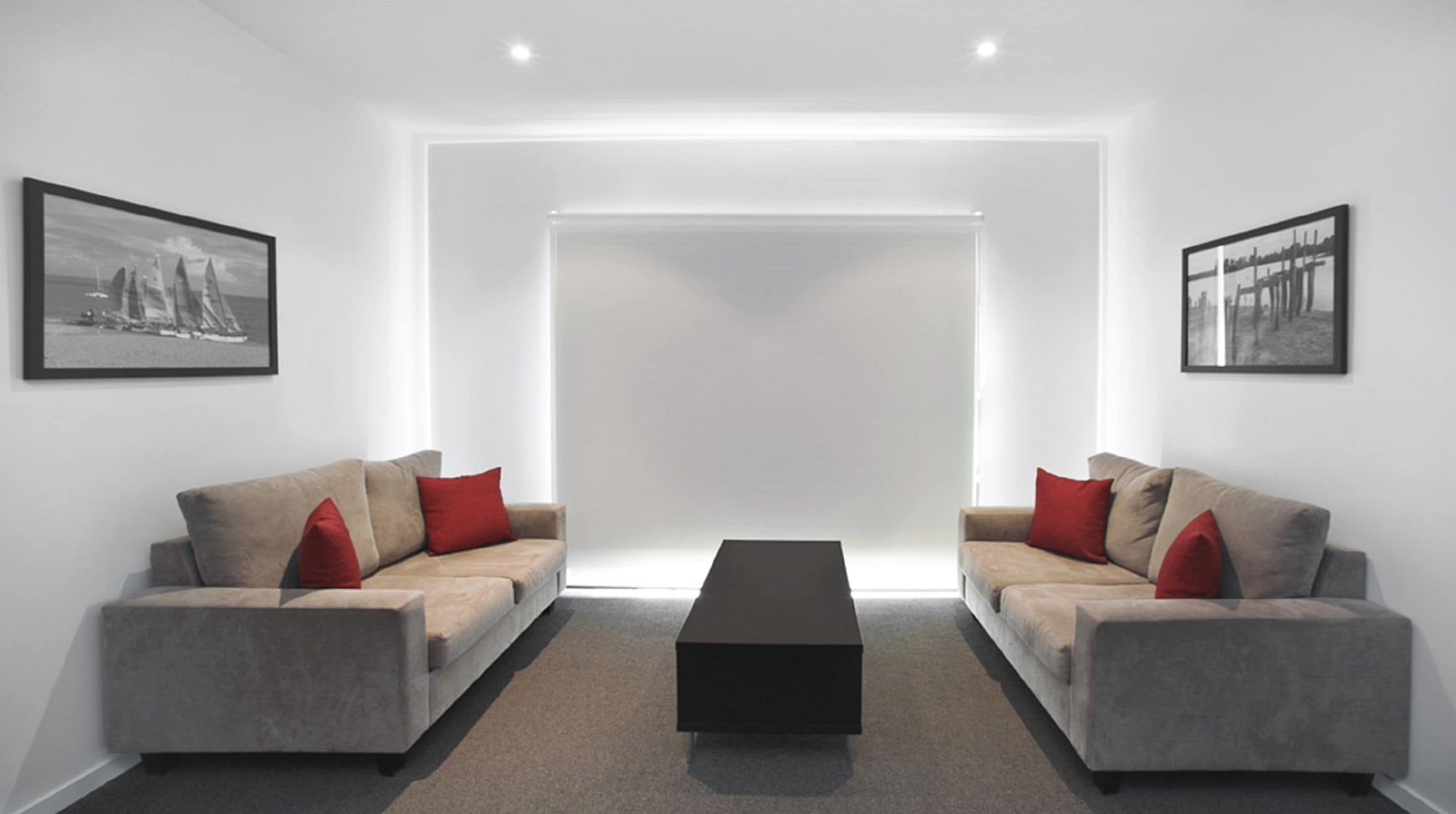 Un salon moderne et minimaliste, avec deux canapés gris, des coussins rouges, une table basse noire et des photographies en noir et blanc encadrées accrochées aux murs.