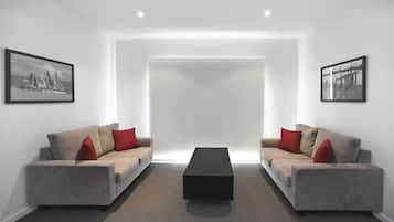 Un salon moderne et minimaliste, avec deux canapés gris, des coussins rouges, une table basse noire et des photographies en noir et blanc encadrées accrochées aux murs.