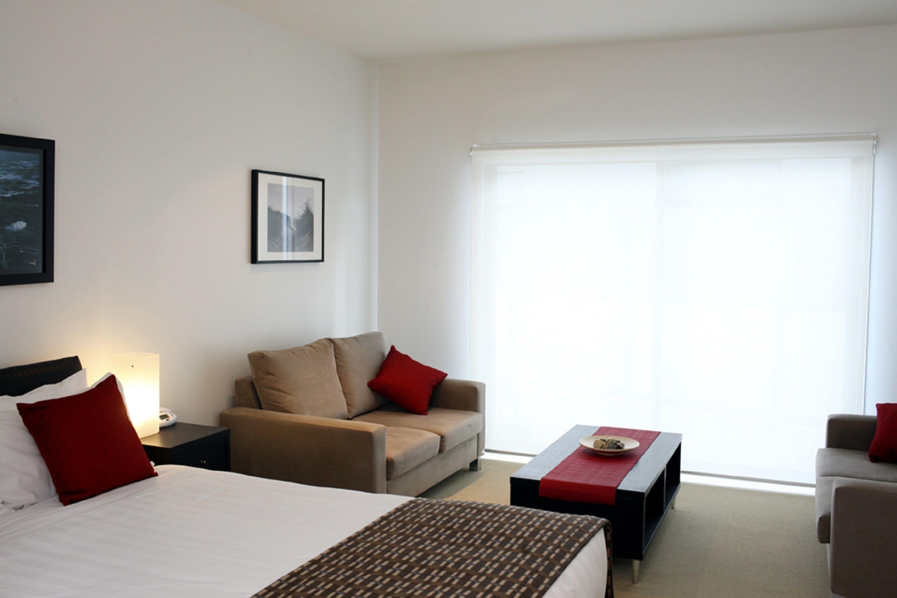 A hotel room with a bed, a sofa, a coffee table, and a window with blinds.