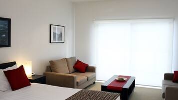 A hotel room with a bed, a sofa, a coffee table, and a window with blinds.