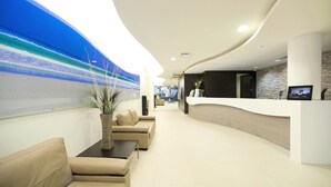 Un área de recepción moderna con un mostrador curvo, una sala de estar con sofás y un mural grande que representa una playa.