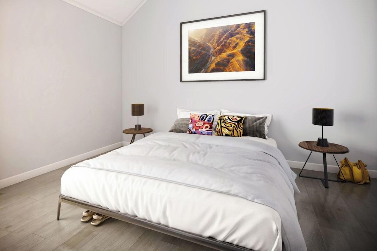 A bedroom with a bed, two bedside tables, a framed picture on the wall, and a pair of shoes on the floor.