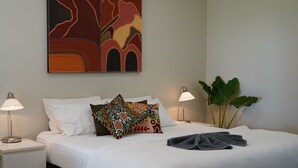 A hotel room with a neatly made bed, two bedside lamps, a large abstract painting, and a potted plant. - Lily Lagoon Resort (Kununurra)