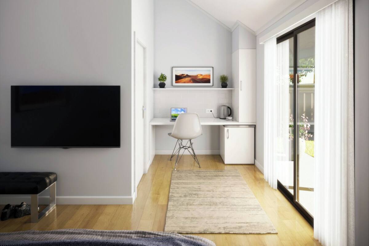 Una sala de estar moderna con un televisor de pantalla plana, un escritorio con una computadora portátil, una silla y un mueble bajo.