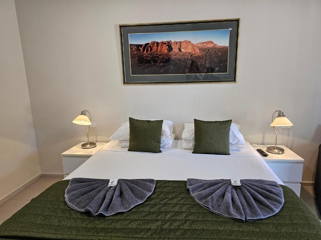 A hotel room with a bed, two nightstands, lamps, a framed landscape photo, and a green bedspread.