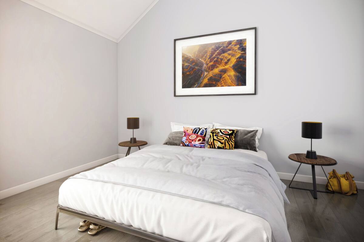 Un dormitorio moderno con una cama grande, un cuadro enmarcado encima y dos mesitas de noche con lámparas.