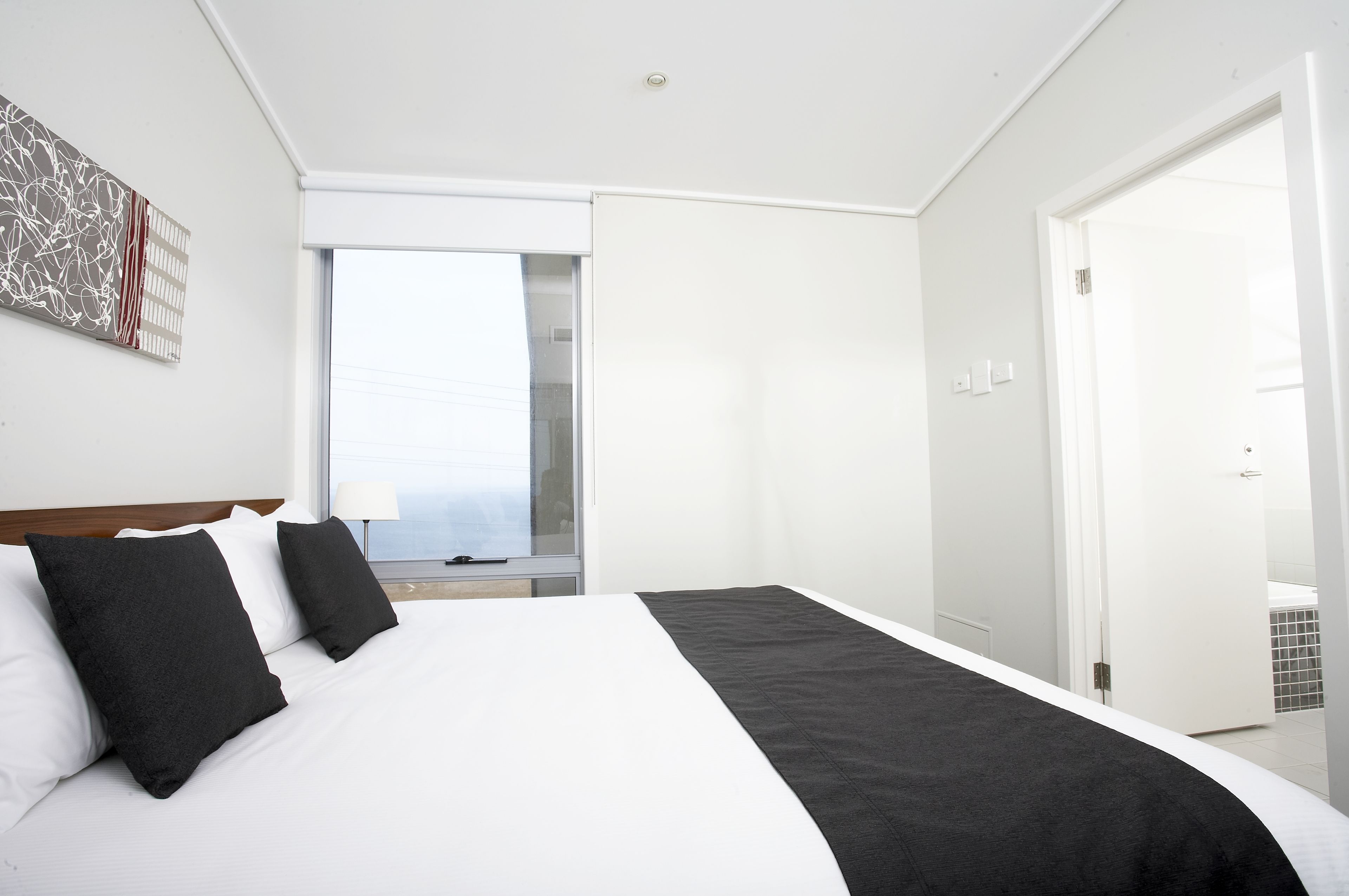 A modern hotel room with a large bed, a window with a view, and a door leading to a bathroom.
