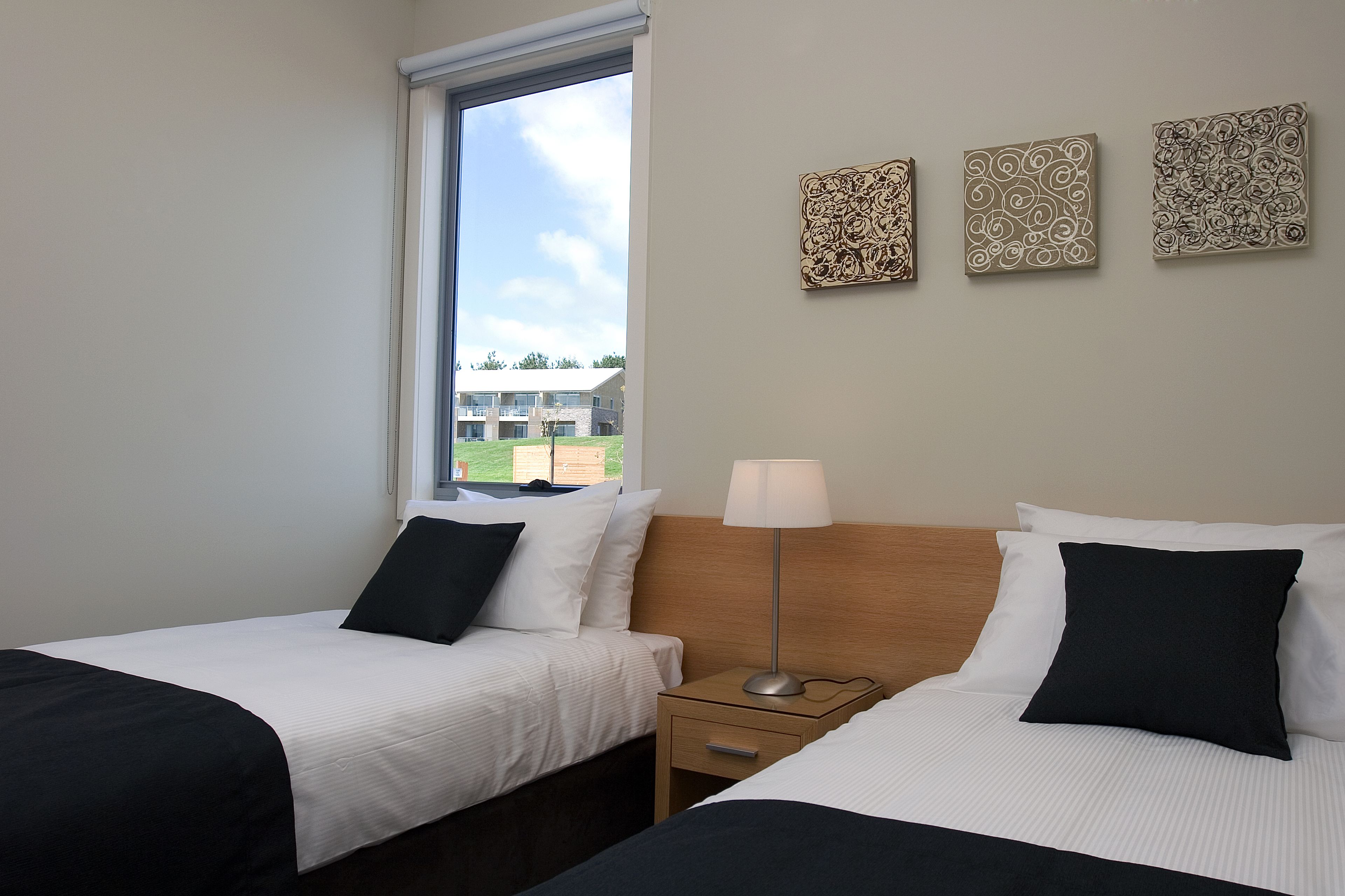 A hotel room with two beds, a window, and three wall-mounted artworks.