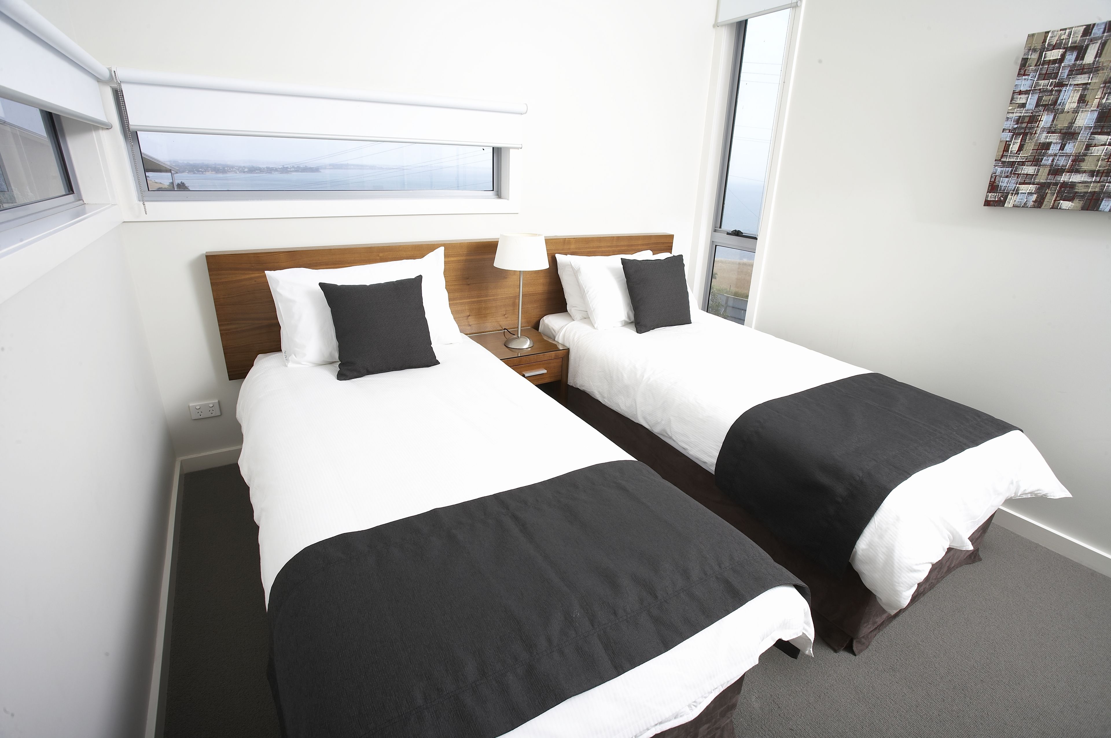 A hotel room with two beds, a window with a view, and a small table with a lamp.