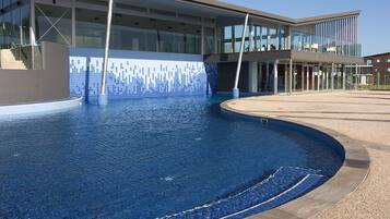 A modern building with a swimming pool, glass windows, and a tiled wall.