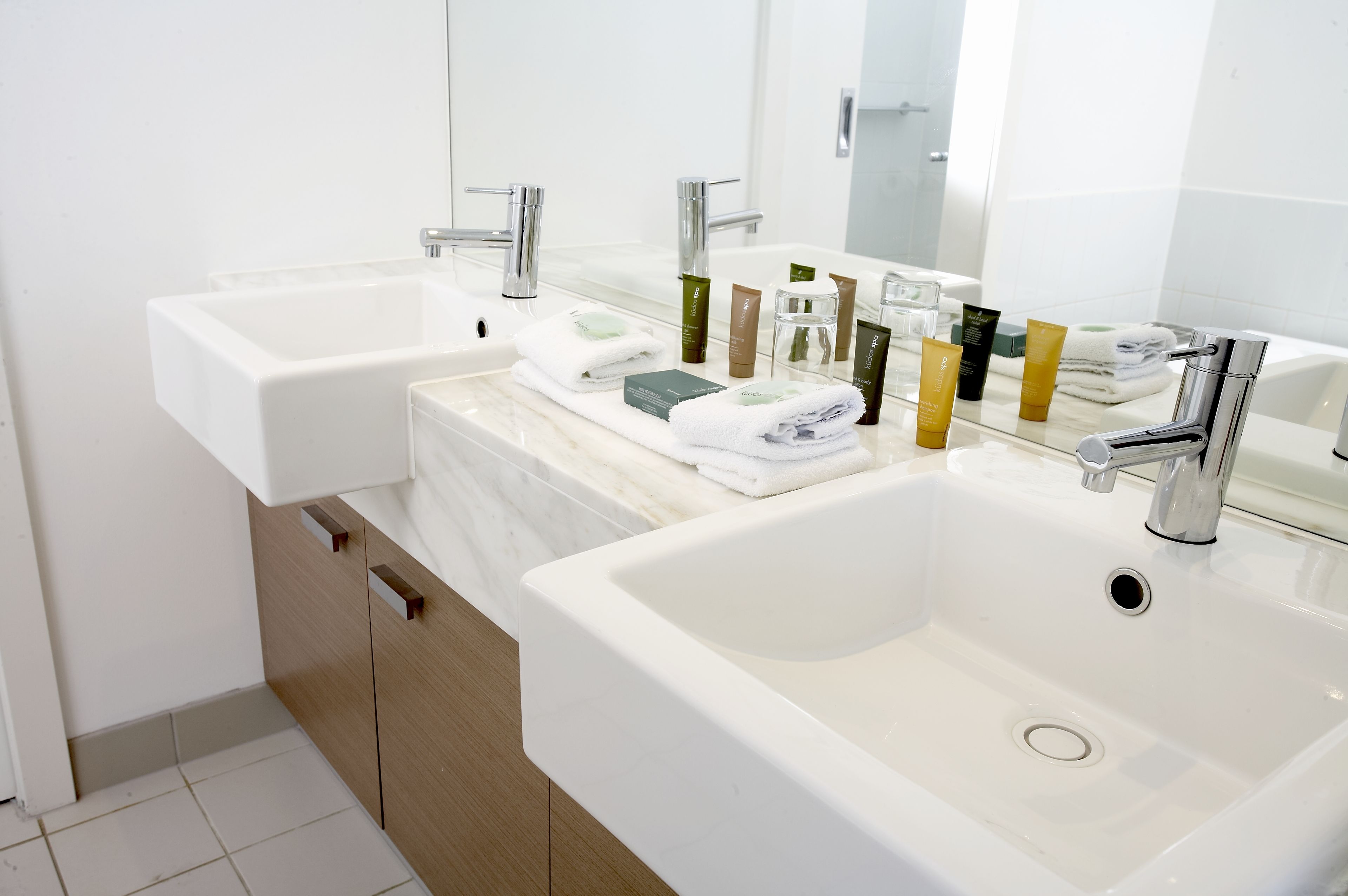 Ein modernes Badezimmer mit zwei Waschbecken, einem großen Spiegel und ordentlich angeordneten Pflegeprodukten.