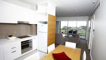 A modern kitchen with white cabinetry, a wooden accent wall, and a dining area with a red cushion.