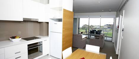 Una cocina moderna con armarios blancos, un muro decorativo de madera y un comedor con un cojín rojo.