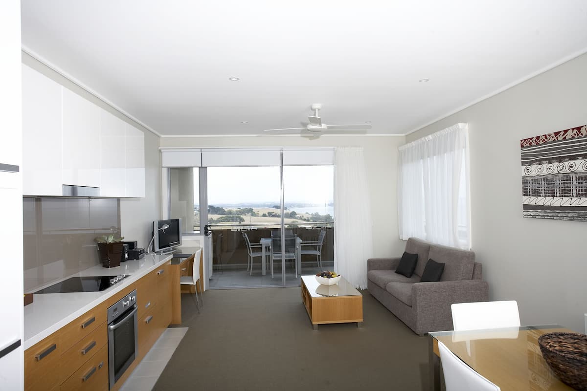 Un apartamento moderno con cocina, comedor y sala de estar. Cuenta con un balcón con vistas, ventilador de techo y televisión de pantalla plana.