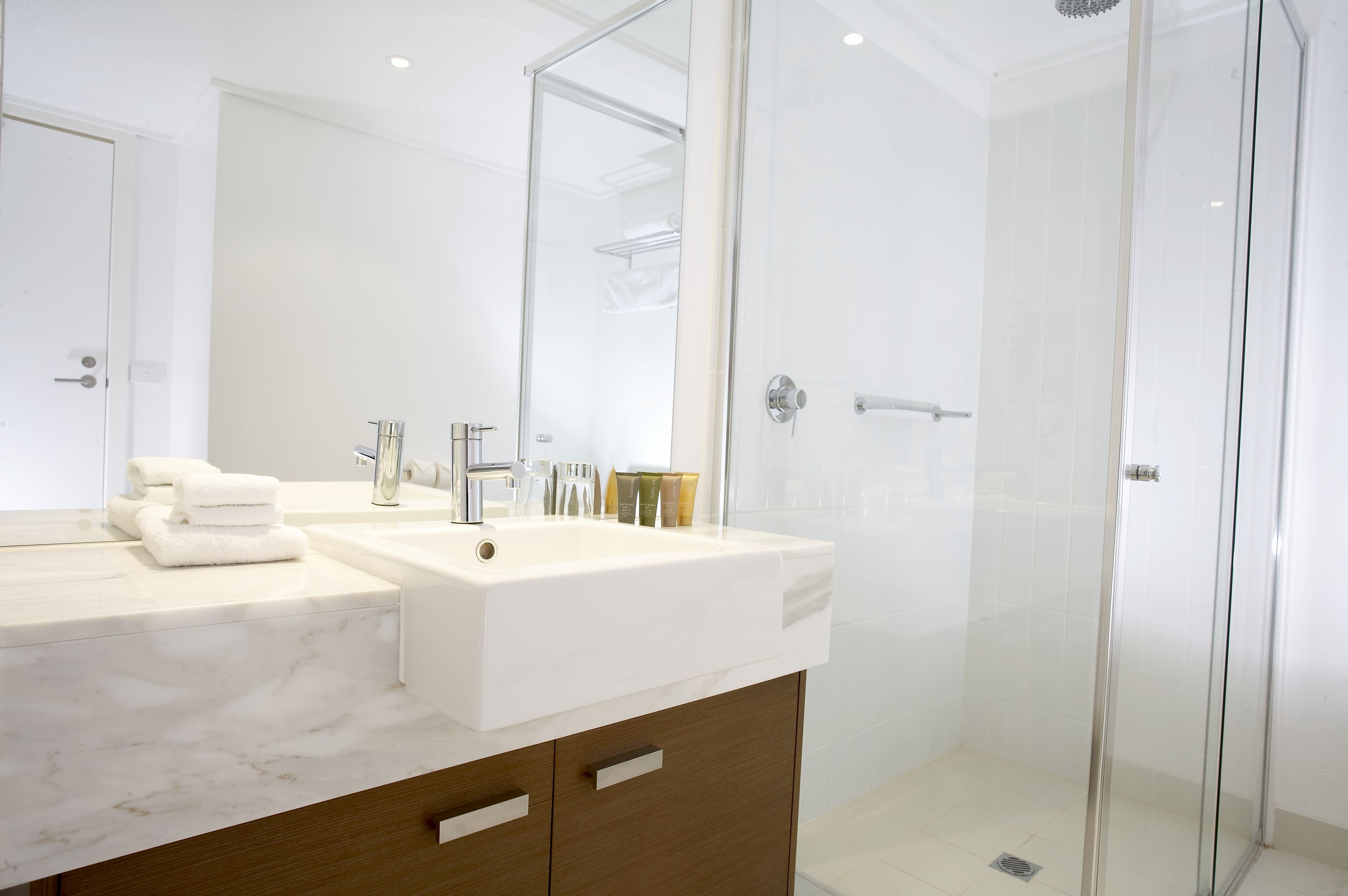 A modern bathroom with a large mirror, two sinks, and a glass-enclosed shower.