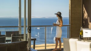 A woman in a white dress and hat standing by a balcony with a view of the ocean.