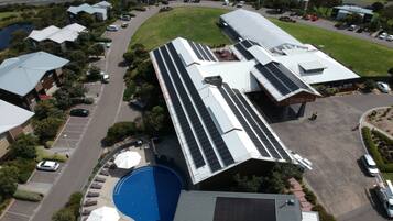 An aerial view of a modern building with a swimming pool, surrounded by parking and greenery.