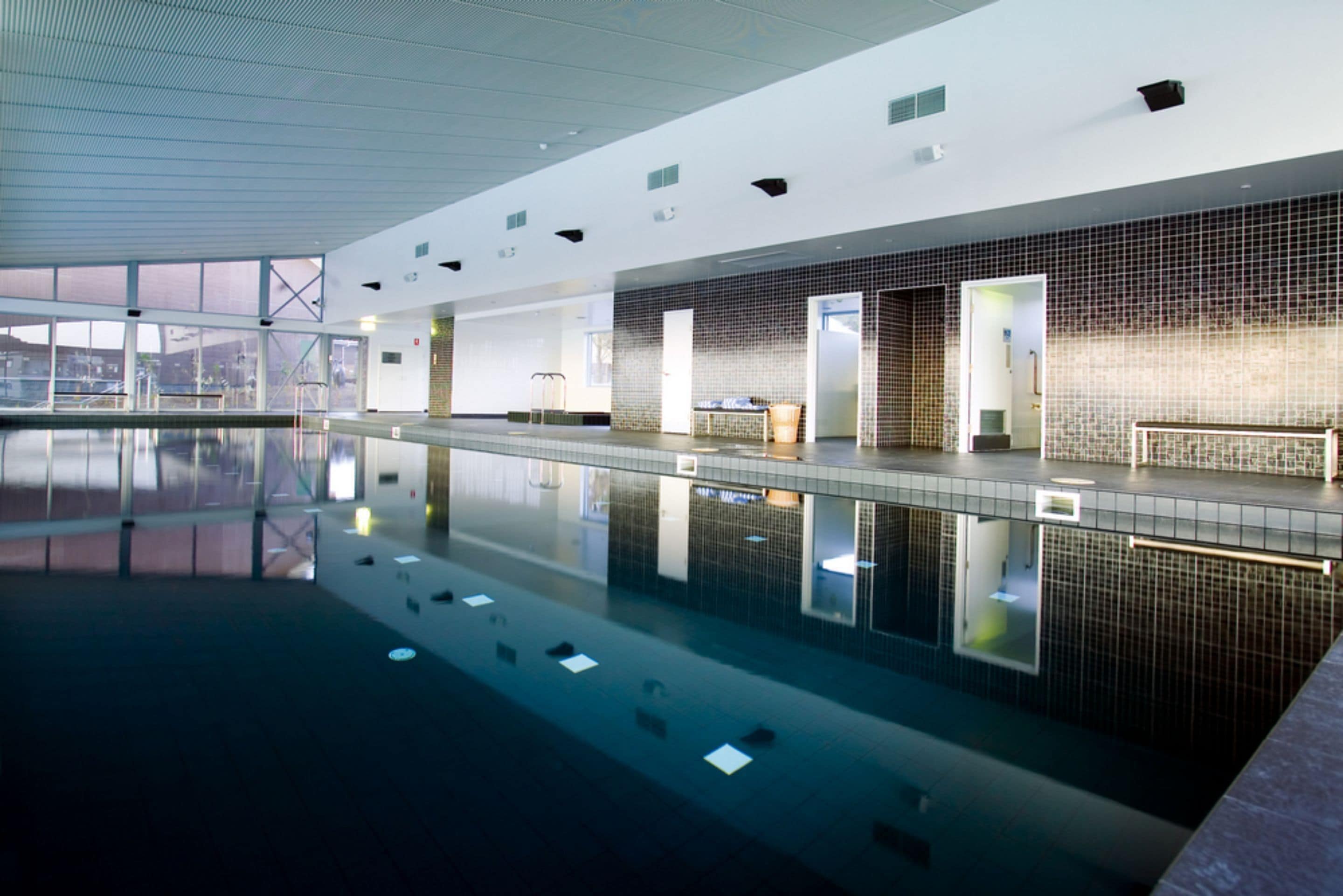 A modern indoor swimming pool with clear water, tiled walls, and a spacious layout.