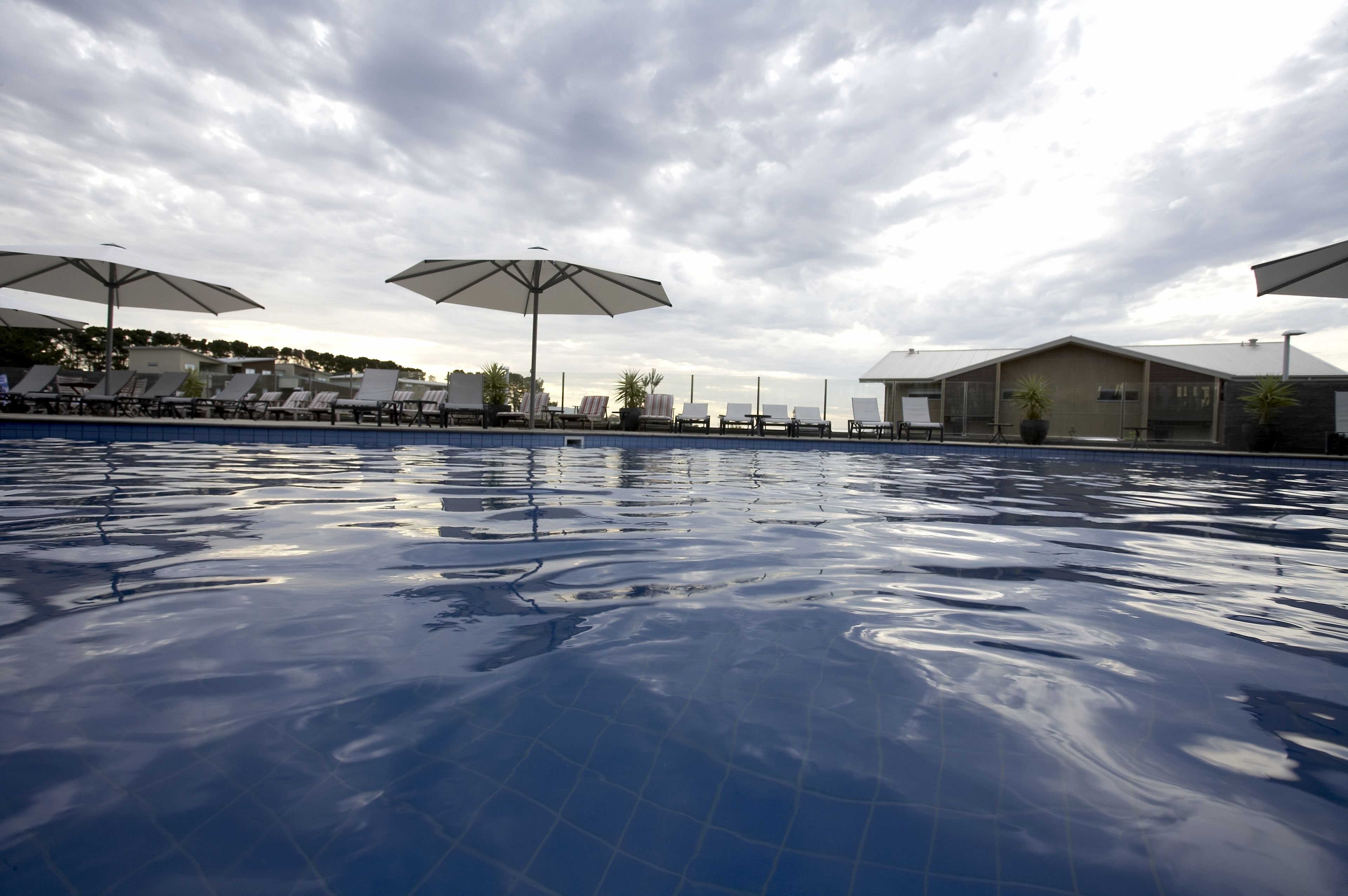 Une piscine entourée de bâtiments, avec des chaises longues et des parasols.