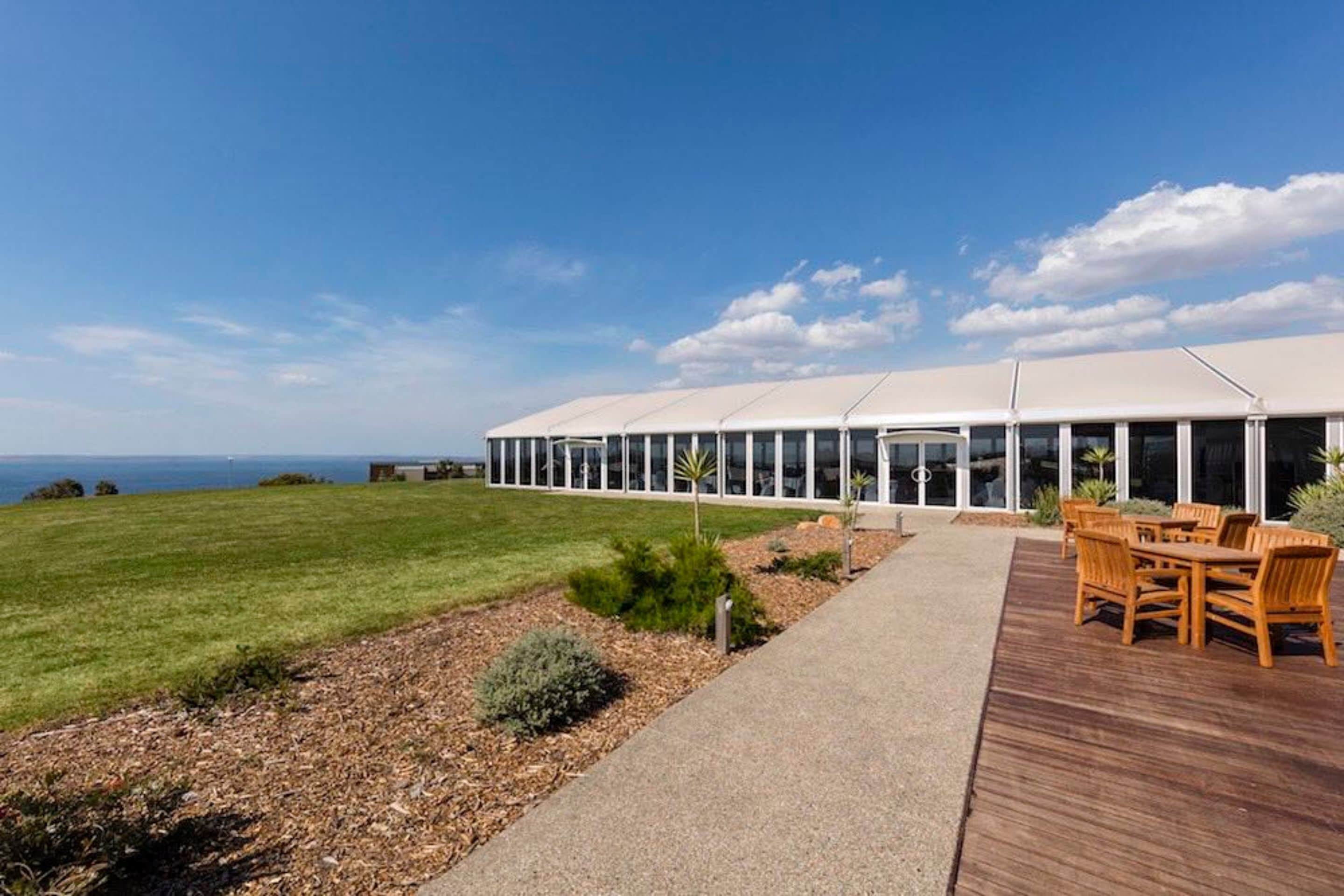 En moderne bygning med en overdækket terrasse, græsplæne og havudsigt.
