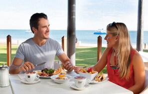 A couple dining at a table with a view of the ocean and a boat in the background.