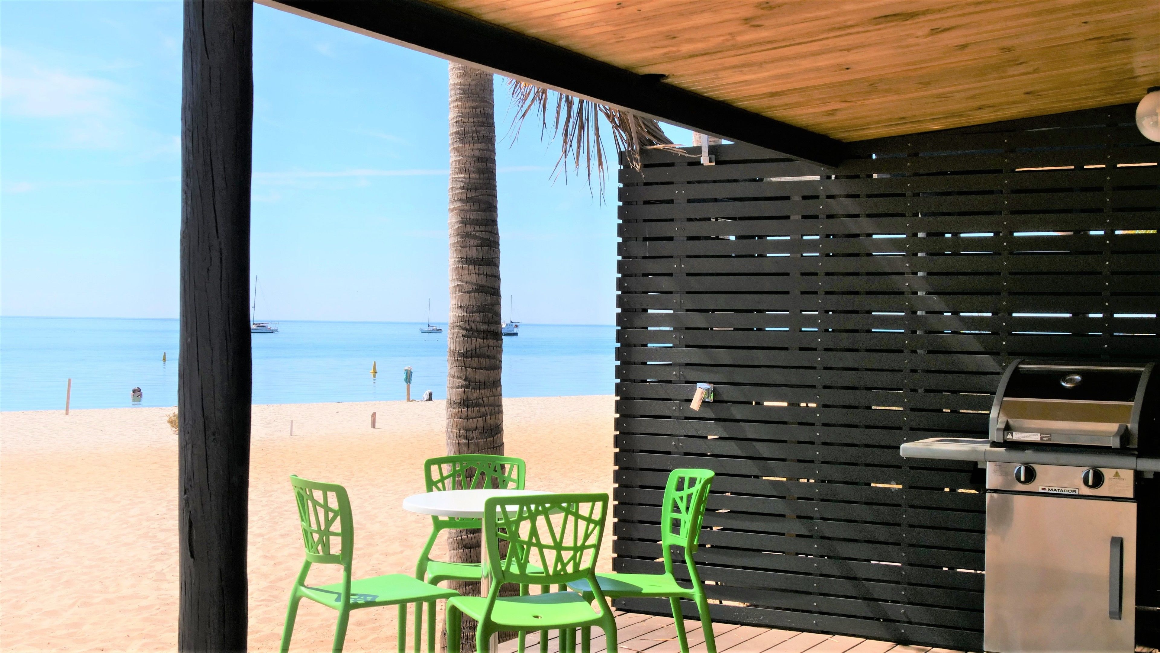A beachside patio with a grill and green chairs, overlooking the sea.
