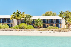 A beachfront hotel with multiple balconies, palm trees, and a sandy beach.