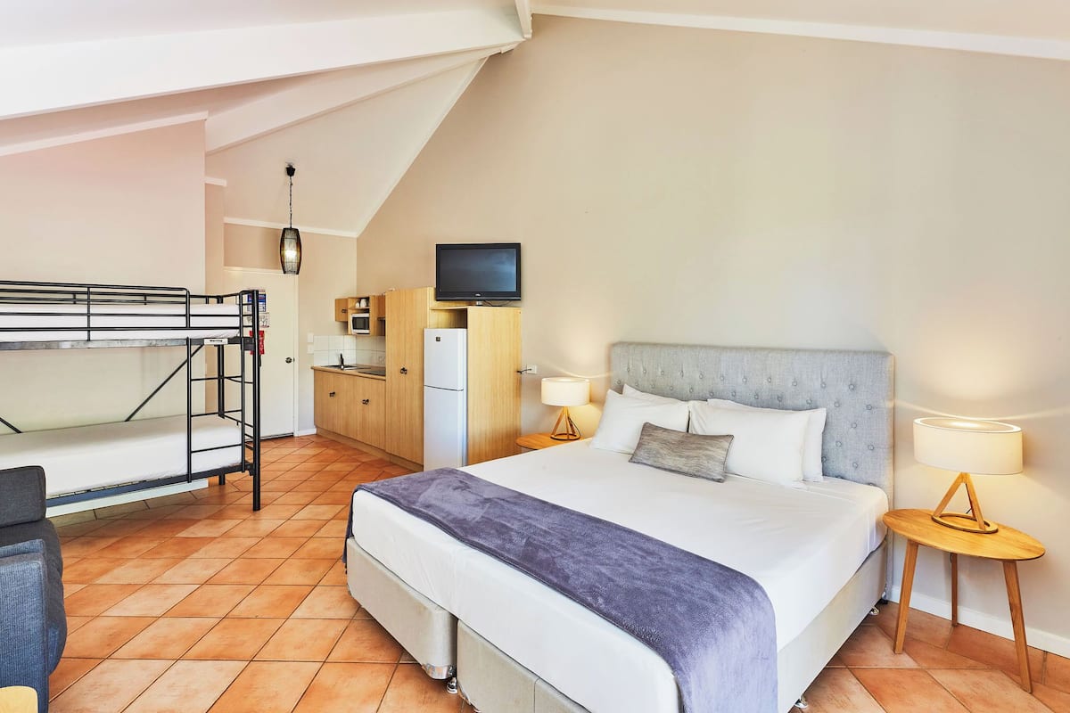 Un dormitorio con una litera, una cama individual, un televisor, un escritorio y una lámpara.
