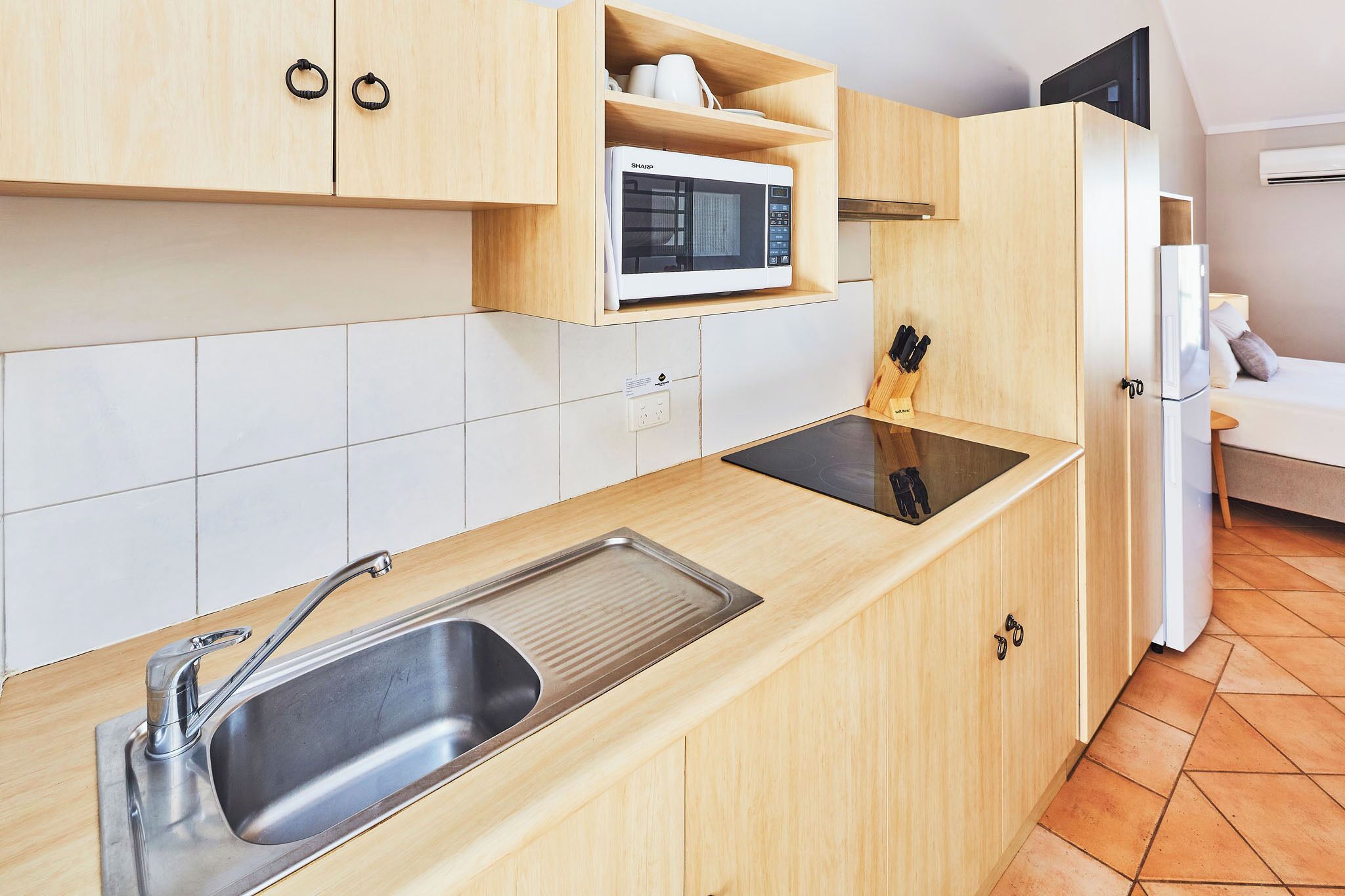 A modern kitchen with wooden cabinets, a stainless steel sink, a microwave, and a refrigerator.