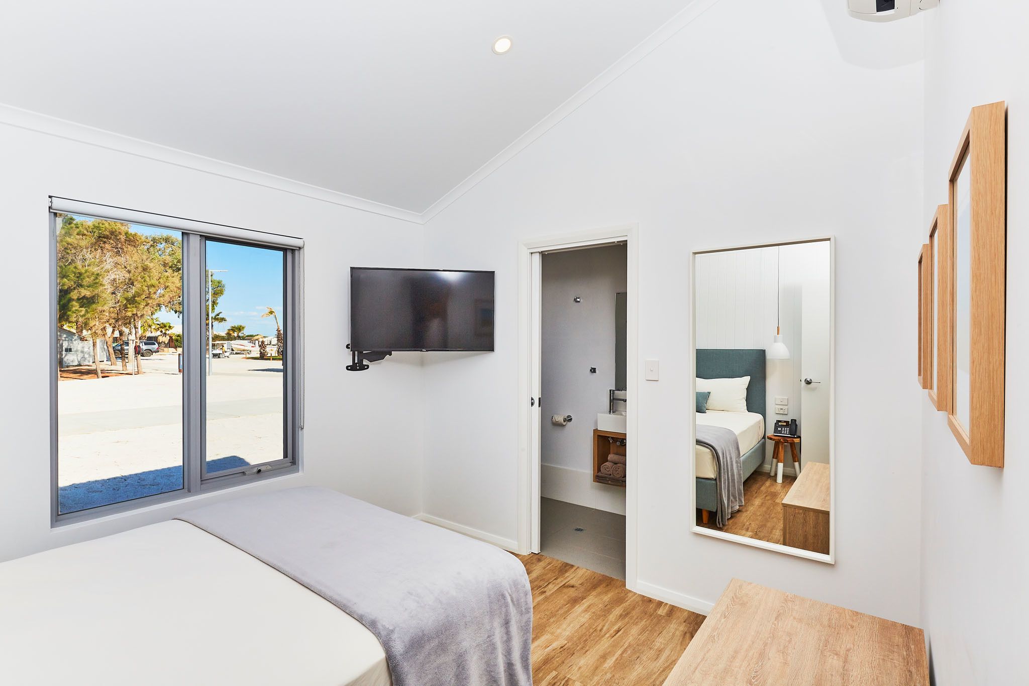 Une chambre moderne avec une grande fenêtre, un téléviseur fixé au mur, un miroir et un plancher en bois.